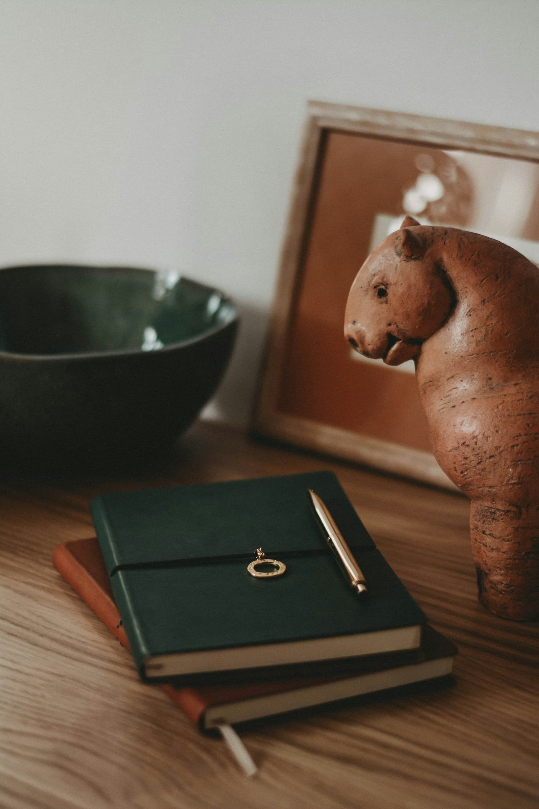 A leather notebook and pen on a wooden desk beside a carved wooden figure